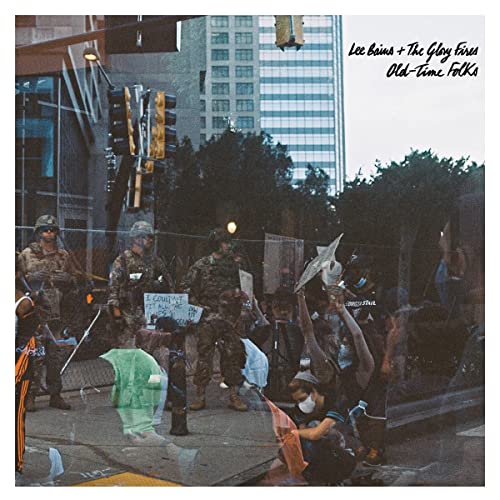 CD cover: protest scene with people, flags, and city buildings.