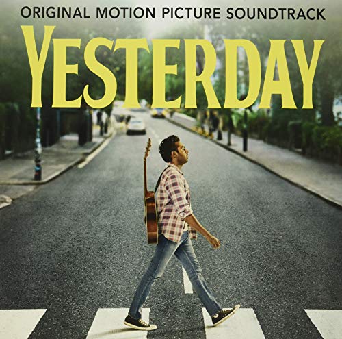 Man in plaid shirt walking across a street with a guitar on his back.