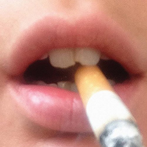 Close-up of a person’s mouth with a lit cigarette between their teeth.