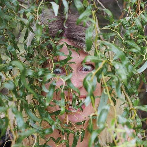Close-up of a person with light hair framed by green foliage.