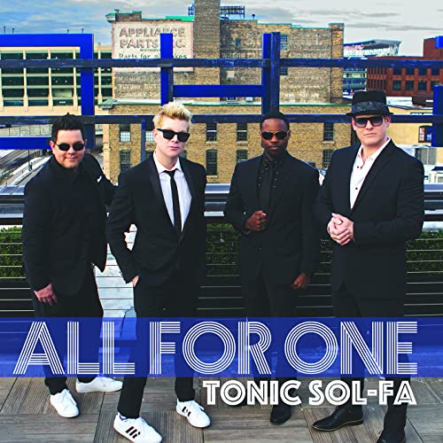 Four men in suits and sunglasses pose on a rooftop.
