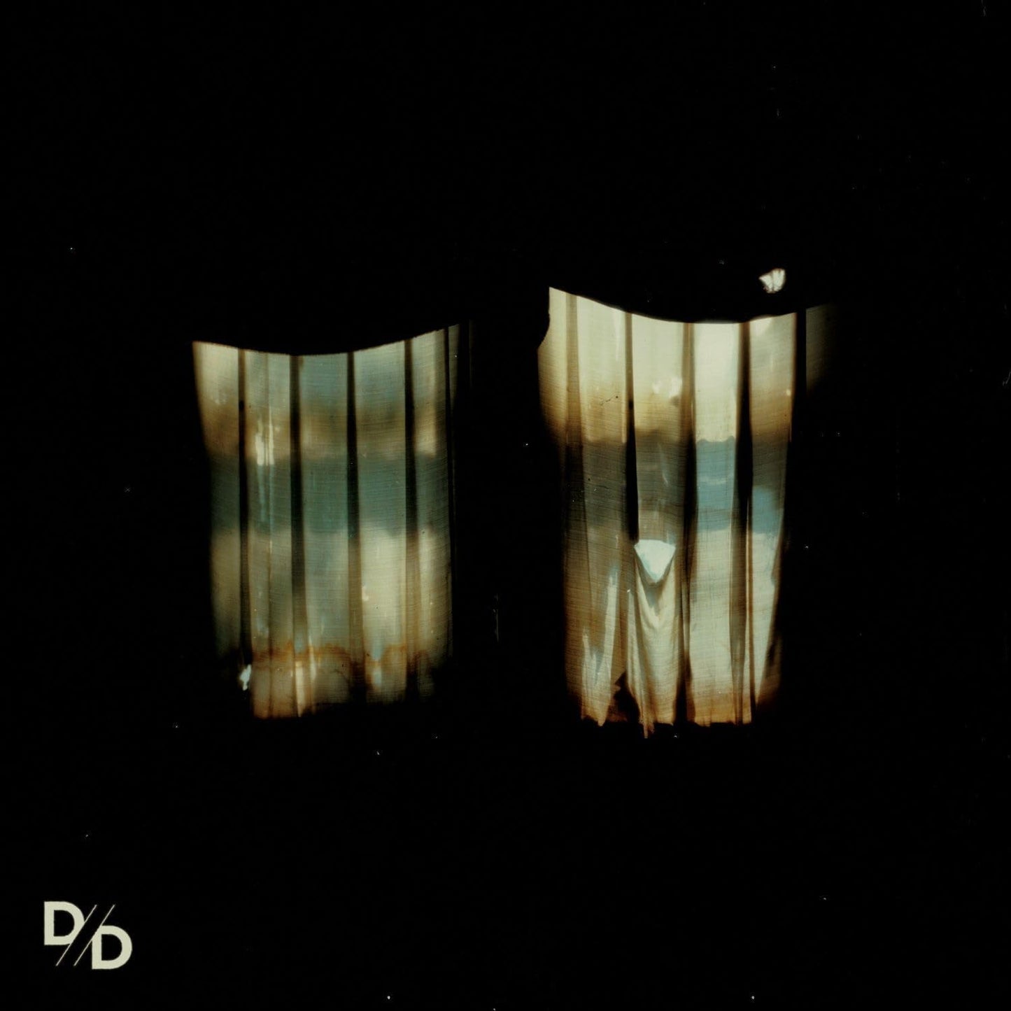 Dark, blurry image of light through curtains with band logo below.