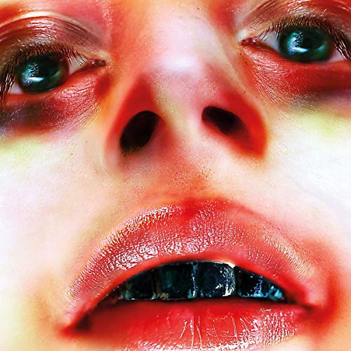 Close-up of a face with red tones and striking dark teeth.