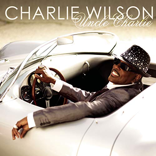 Charlie Wilson in a silver convertible, wearing a suit and hat.