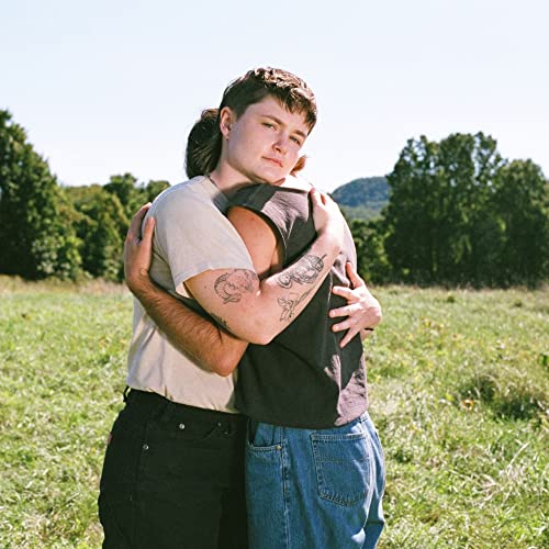 Two people embracing in a grassy field with trees in the background.