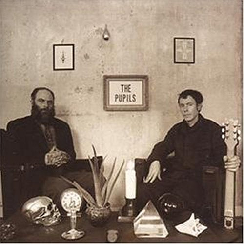 Two men sit before a wall with framed pictures and a The Pupils sign.