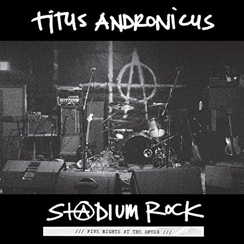 Black and white photo of a stage with instruments and an anarchy symbol backdrop.