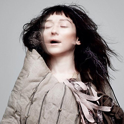 A woman with dark hair and eyes closed against a plain grey background.
