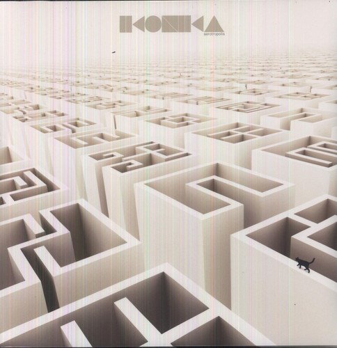 A small black cat walks along the wall of a vast, white geometric maze.