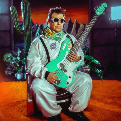 Man in spacesuit playing a teal electric bass guitar indoors.
