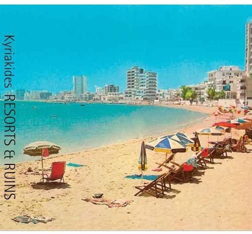 Beach scene with lounge chairs, umbrellas, and a coastal city backdrop.