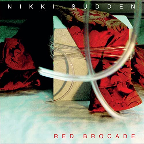 Album cover for Nikki Sudden’s “Red Brocade” featuring red brocade fabric.