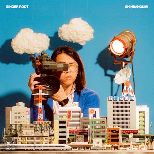 Album cover with a person filming a miniature city landscape.