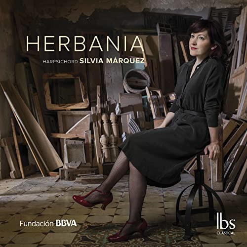 Silvia Márquez sits on a stool amidst antique furniture, album cover.