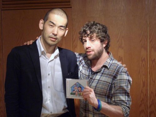 Two men holding a CD case with illustrated cover art.