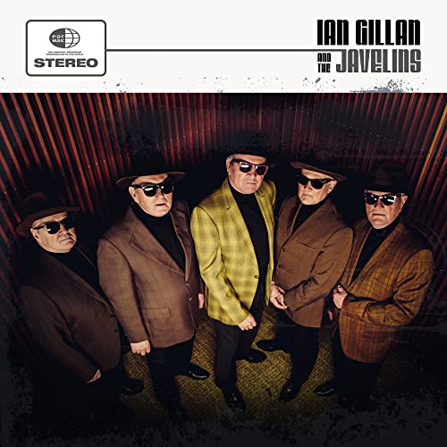 Six men in suits and hats with sunglasses pose against a wall.
