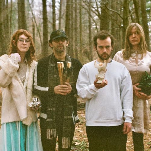 Four people in a forest hold small, ornate sculptures.