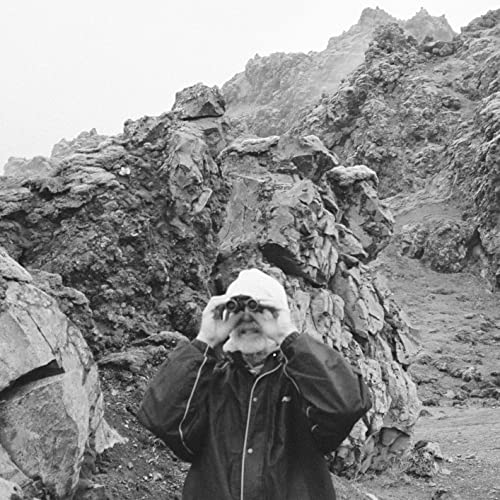 Black and white photo of a bearded man with binoculars in mountains.