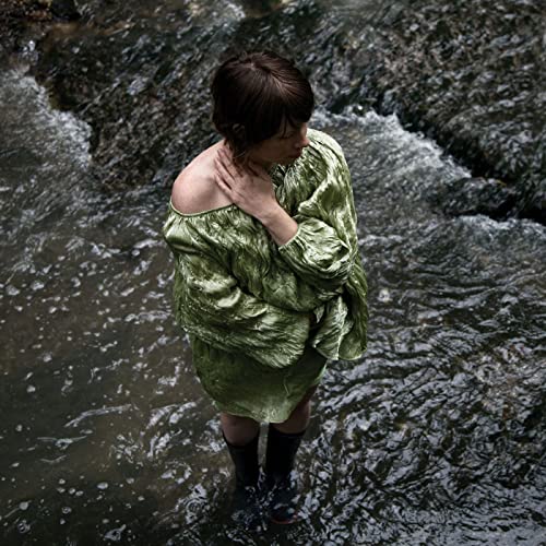 Woman in green dress standing in shallow, flowing water.