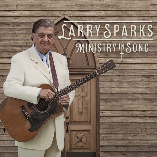 Larry Sparks holds a guitar in front of a wooden church door.
