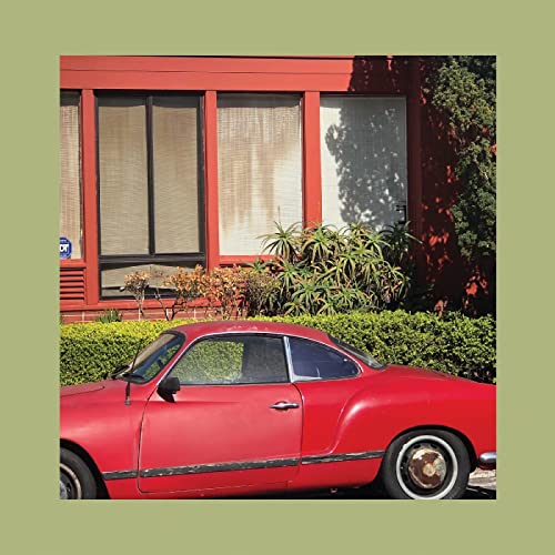 Red car parked in front of a red building with green shrubbery.