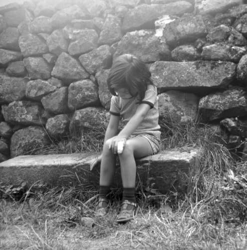 Black and white photo of a young girl sitting against a stone wall.