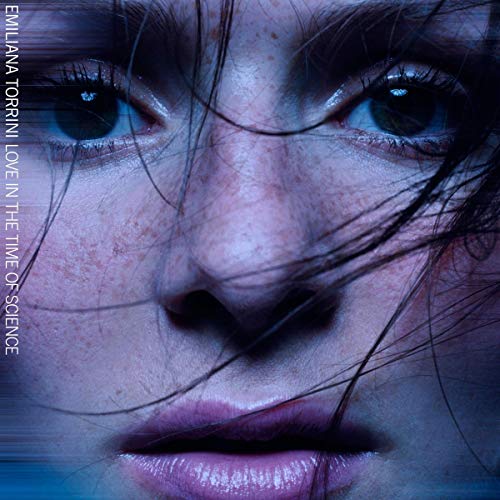 Close-up portrait of a woman with freckles, dark hair, and blue-toned lighting.