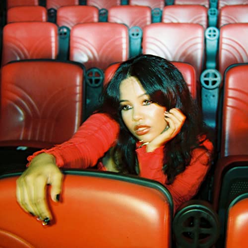 Young woman with long dark hair sits amongst red theater seats.