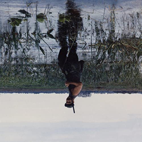 Upside-down figure in water, holding a knife, with reeds and sky reflection.