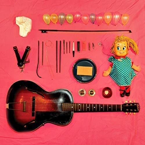 Still life of musical instruments, doll, and balloons on red fabric.