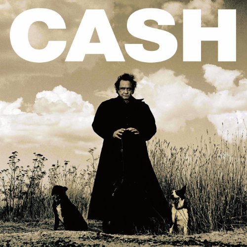 Johnny Cash in a black coat standing in a field with two dogs.