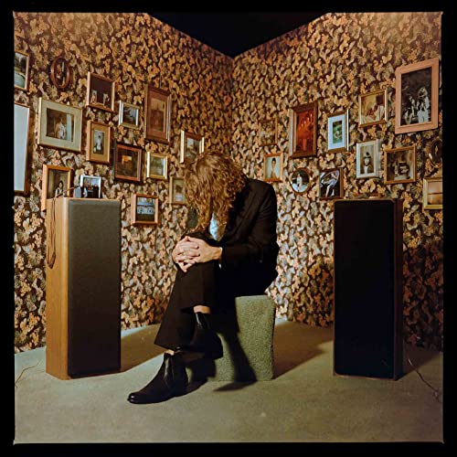 Person with long hair sits in a room filled with framed photos.