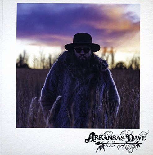 Man in a fur coat and hat stands in a field.