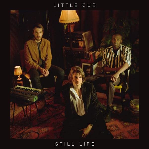 Three musicians sit in a dimly lit, patterned room.