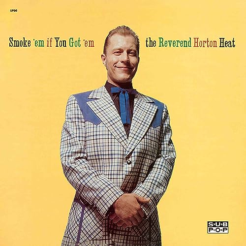 Man in a plaid western suit and bolo tie against a solid yellow background.