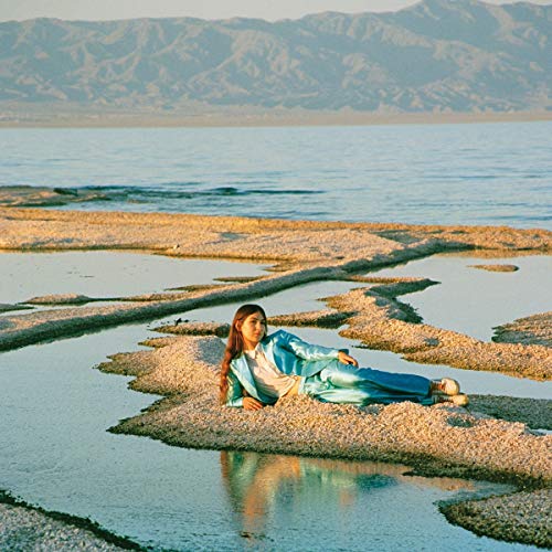 Woman in blue lies on rocky shore with mountains in background.