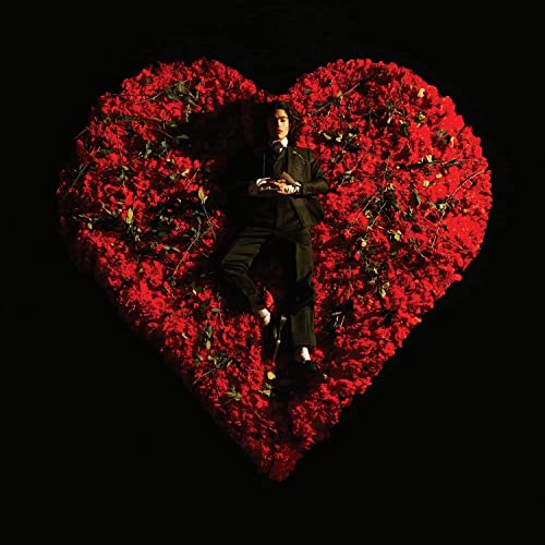 Conan Gray stands within a heart shape formed of red roses.