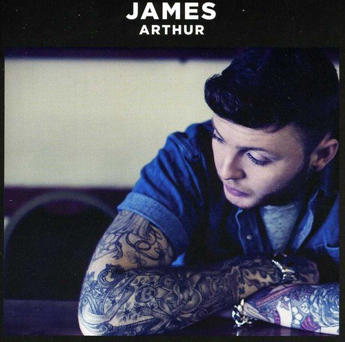 Man with dark hair and tattoos on arms leaning on surface, looking down.