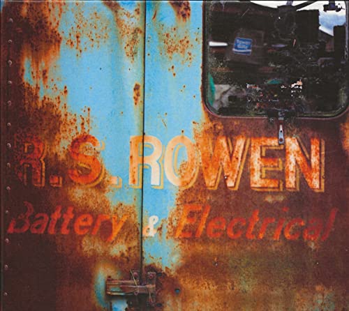 Rusty blue metal door with faded "Rowen Battery & Electrical" text.
