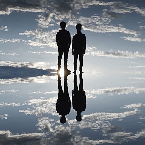Silhouettes of two people standing against a cloudy sky reflected in water.