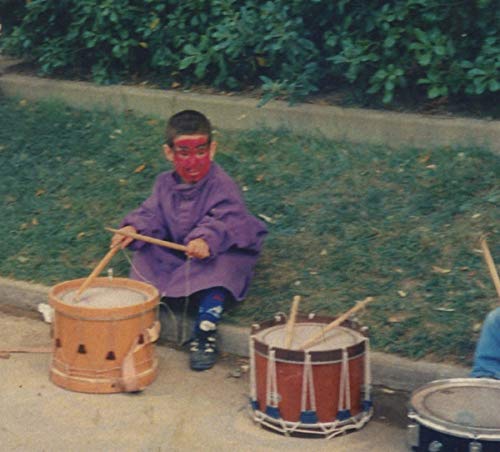 Young child in face paint playing drums outdoors.