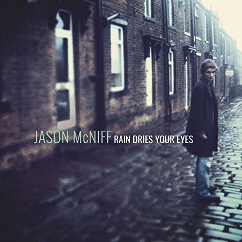 CD cover: man standing on a wet cobblestone street, brick buildings.