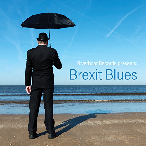 Man in suit with umbrella stands on beach, looking at sea.