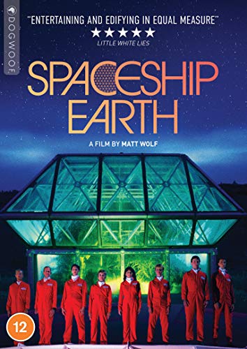 Nine people in orange jumpsuits stand before a large glass pyramid at night.