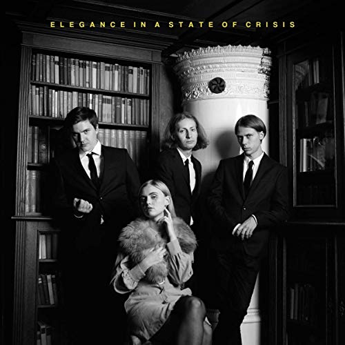 Three men in suits and one woman in a fur stole pose in a library.