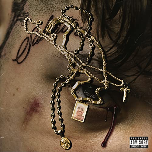 Close-up of a person's face with gold chains, a pendant, and a blood tear.