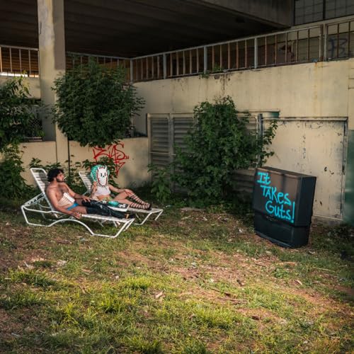 Two people lounge near a vintage TV with graffiti, outdoors.