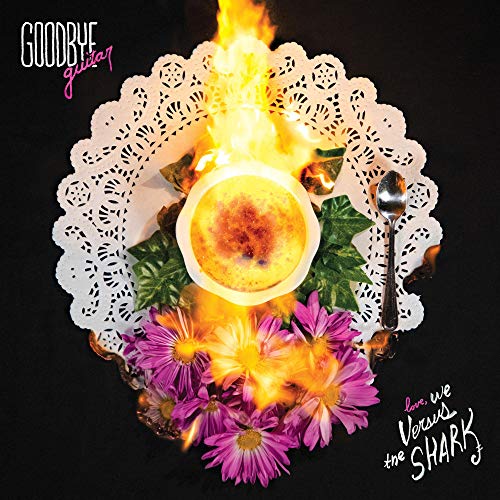 Burning guitar on a doily with flowers, fruit, and silverware.