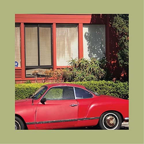 Red vintage car parked in front of a red building with greenery.
