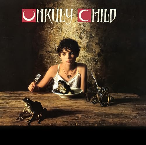 A child sits at a wooden table with three frogs and silverware.